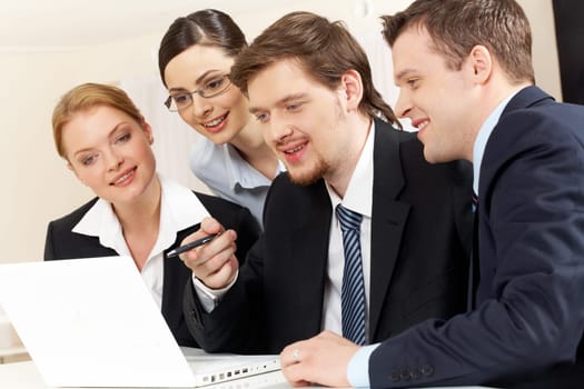 Portrait of friendly workteam looking at monitor of laptop while confident businessman pointing at screen
