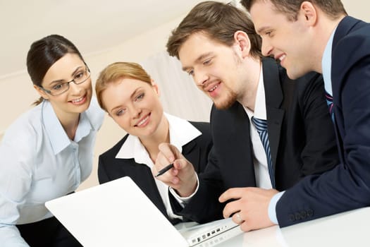 Portrait of friendly workteam looking at monitor of laptop while confident businessman pointing at screen