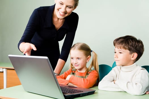 Image of two pupils looking at laptop monitor while teacher pointing at it