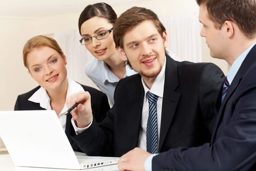 Portrait of friendly workteam discussing project while confident businessman pointing at laptop screen