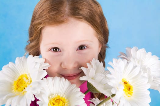 Portrait of cute girl looking from behind spring flowers on blue background