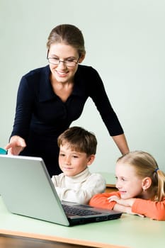 Photo of elegant teacher explaining new topic by pointing at laptop monitor while children looking at it