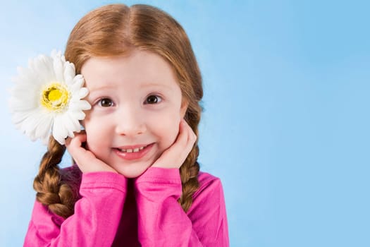 Portrait of charming girl with flower in hair touching her face over blue background