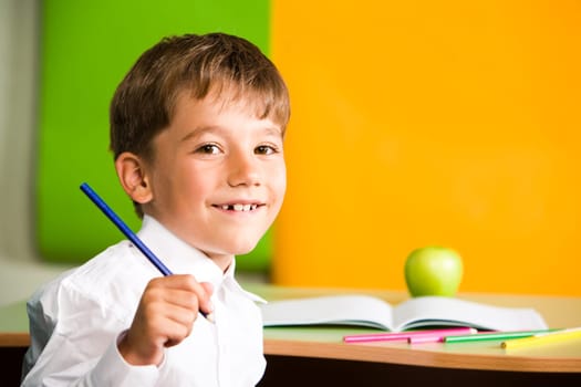 Portrait of handsome schoolboy holding pencil in hand and looking at camera