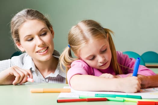 Portrait of diligent girl drawing something under tending of her teacher