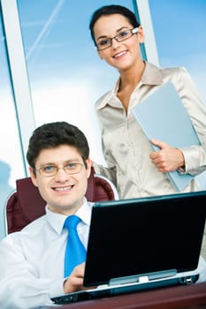 Portrait of confident boss sitting in workshop with smart businesswoman standing near by