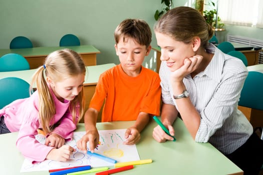 Image of confident teacher looking at girls picture with cute boy near by