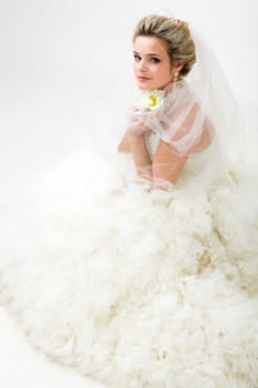 Photo of elegant bride in fashionable wedlock with flower in hand sitting and looking at camera