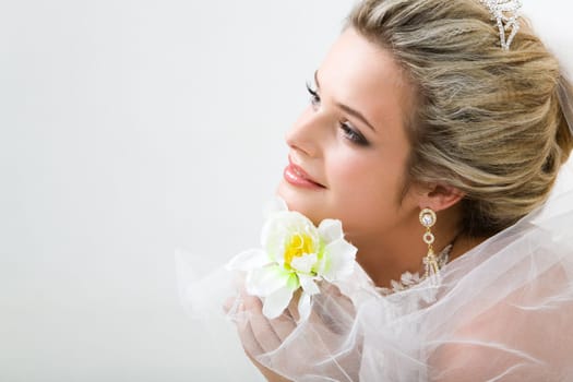 Close-up of charming bride holding flower by her chin and looking straight