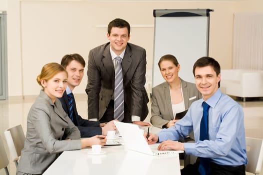 Portrait of several confident colleagues looking at camera with smiles at workplace