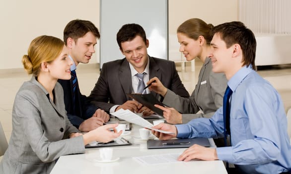 Portrait of friendly colleagues looking at each other while confident woman sharing her idea with co-workers on background