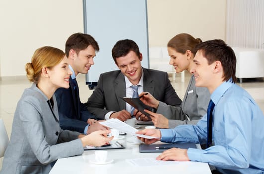 Portrait of friendly colleagues looking at each other while confident woman sharing her idea with co-workers on background