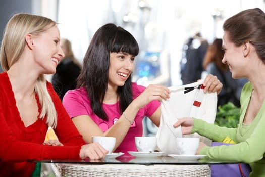 Three young women sitting in cafe and discussing new purchase