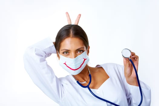 Portrait of assistant in mask with big smile on it keeping two fingers behind head and looking at camera
