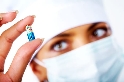 Close-up of nurse hand holding colorful pill between thumb and forefinger