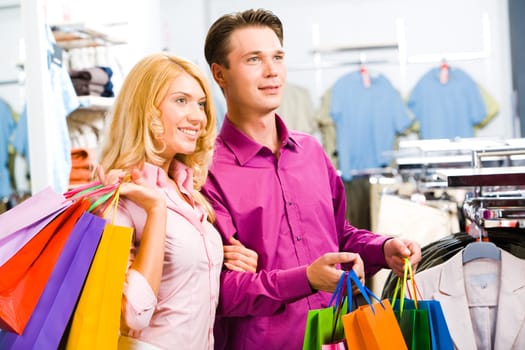 Portrait of modern couple with shopping bags looking at clothes in the trade center
