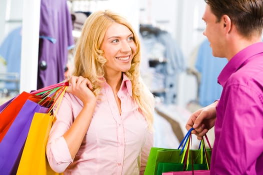 Portrait of happy blond woman looking at smiling man and holding bags in hands