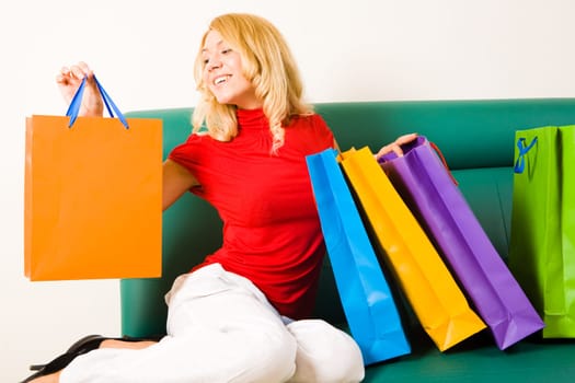 Portrait of fashionable woman holding orange bag in hand and looking at it with satisfied expression