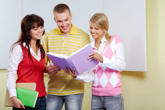 Portrait of three friends standing in classroom and discussing passage from book