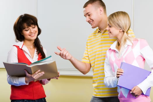 Image of handsome guy with his girlfriend near by pointing at book in another girls hands and explaining something