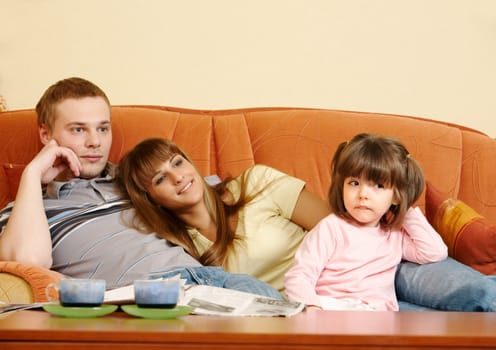 Happy couple and their daughter relaxing on sofa and watching TV