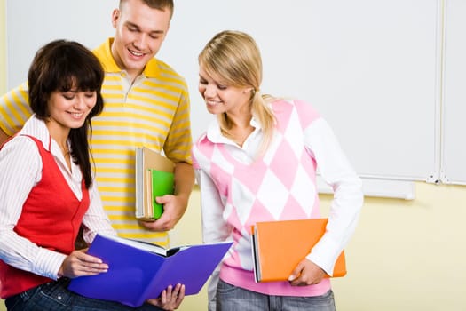 Image of three teens looking into textbook with smiles while preparing for the lesson