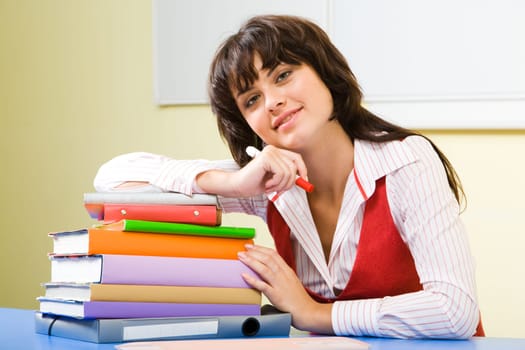 Portrait of positive girl putting her arm onto pile of books and looking at camera with smile