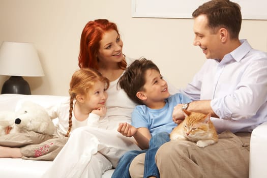 Curious children and woman looking attentively at handsome man while relaxing on sofa