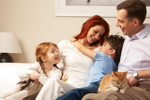 Photo of cute boy embracing his pretty mother surrounded by playful daughter and their father
