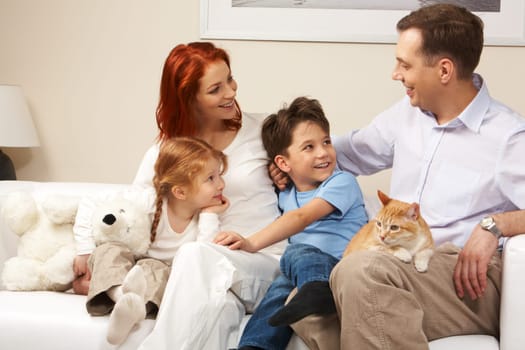 Curious children and woman looking attentively at handsome man while relaxing on sofa