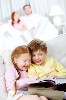 Portrait of happy children reading book while sitting on sofa at home