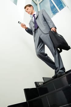 Below view of businessman in suit with cellular phone and bag in hands walking downstairs