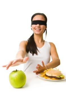 Portrait of young girl in blindfold stretching her hand towards green apple and putting away fast food