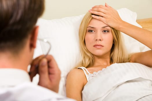 Image of pretty woman in bed touching her forehead and looking at doctor