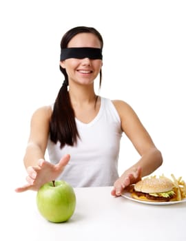 Portrait of young girl in blindfold stretching her hand towards green apple and putting away fast food
