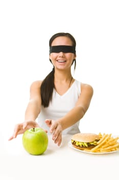 Portrait of young girl with her eyes folded deciding what to eat: an apple or fast food