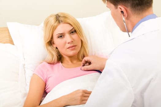 Photo of sad woman lying in bed while male doctor examining her with stethoscope