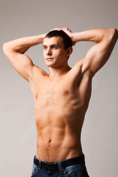 Image of shirtless man in jeans looking forwards with his hands on top of head
