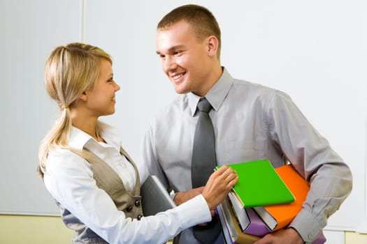 Portrait of pretty girl looking at handsome guy while taking book from stack that he holds