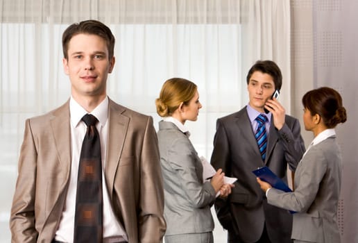 Portrait of handsome employer smiling at camera with consulting staff on background