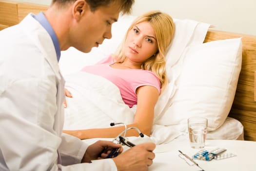 Sick female lying in bed and looking at male doctor while he prescribing her medication