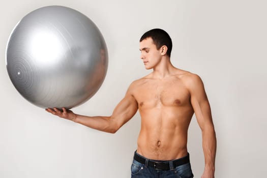 Portrait of shirtless man in jeans holding big ball on hand