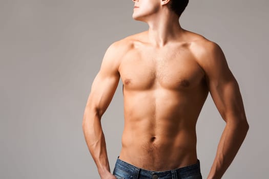 Torso of shirtless man in jeans posing in front of camera