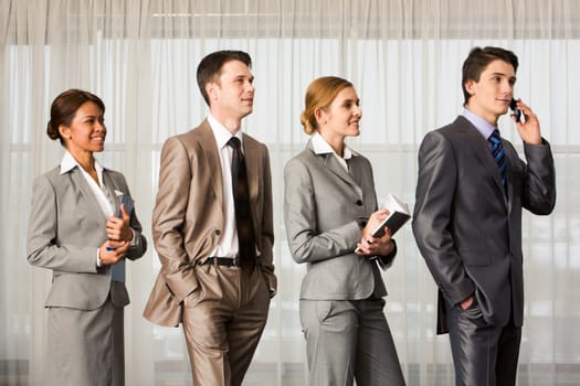 Contemporary business people standing in line and looking aside with smiles