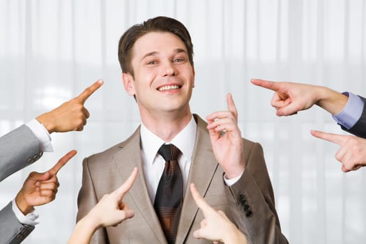 Successful businessman pointing upwards and smiling at camera surrounded by several forefingers