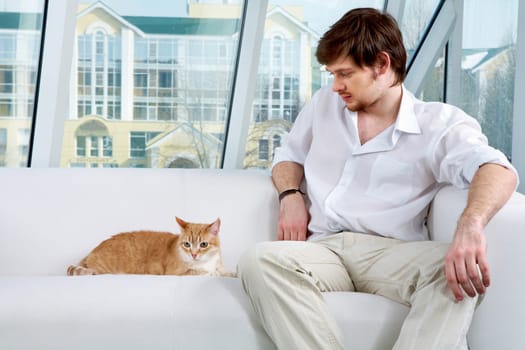 A man sitting on sofa and looking at a cat