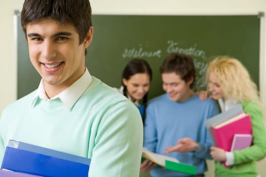 Portrait of cheerful lad with textbooks looking at camera on background of reading groupmates