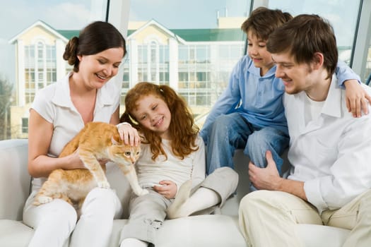 Photo of cute girl caressing pet on her mothers knees while father and boy looking at it