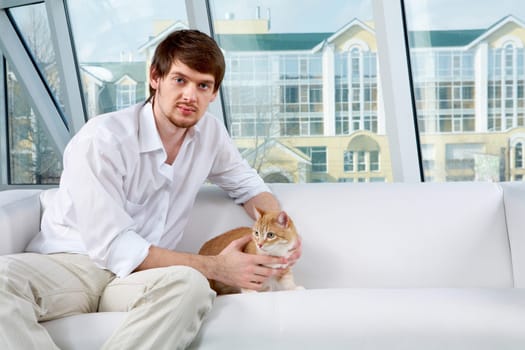 A man sitting on sofa with a cat and looking at camera