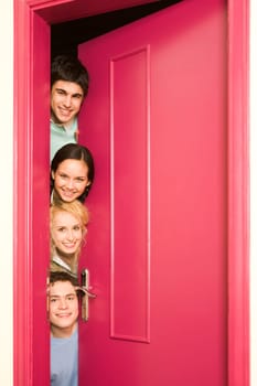 Portrait of happy students looking from behind door at camera with smiles